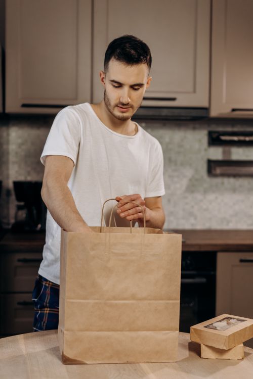 Free Adult male unpacking a takeout box from a paper bag in a modern kitchen. Stock Photo