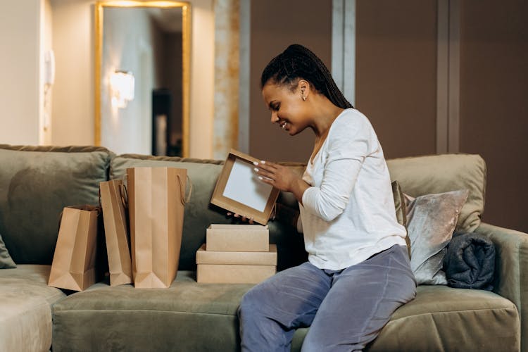 Woman Sitting On Couch Opening Brown Boxes And Paper Bags