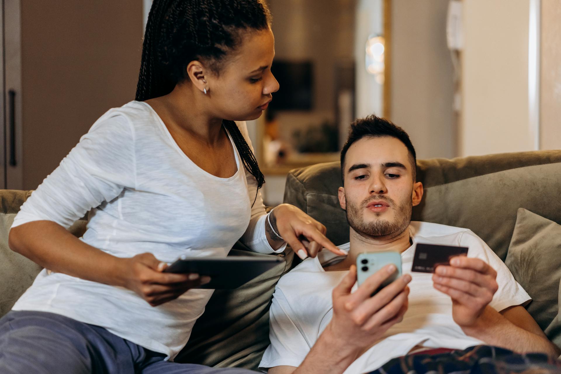 A couple comfortably online shopping at home using a smartphone and tablet for digital purchases.