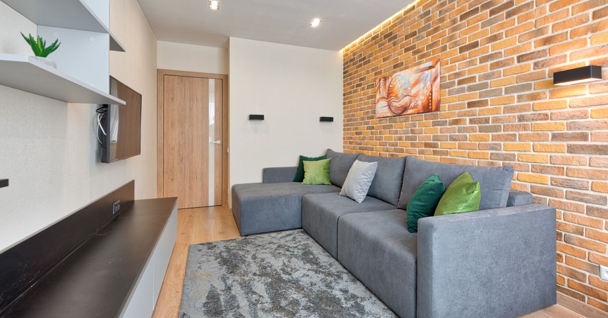 Stylish living room featuring a gray L-shaped sofa, brick wall, and modern decor.