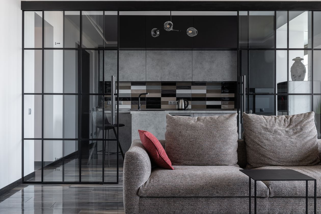 A dark solid half-wall partition between a home office desk area and a bedroom with grey curtains