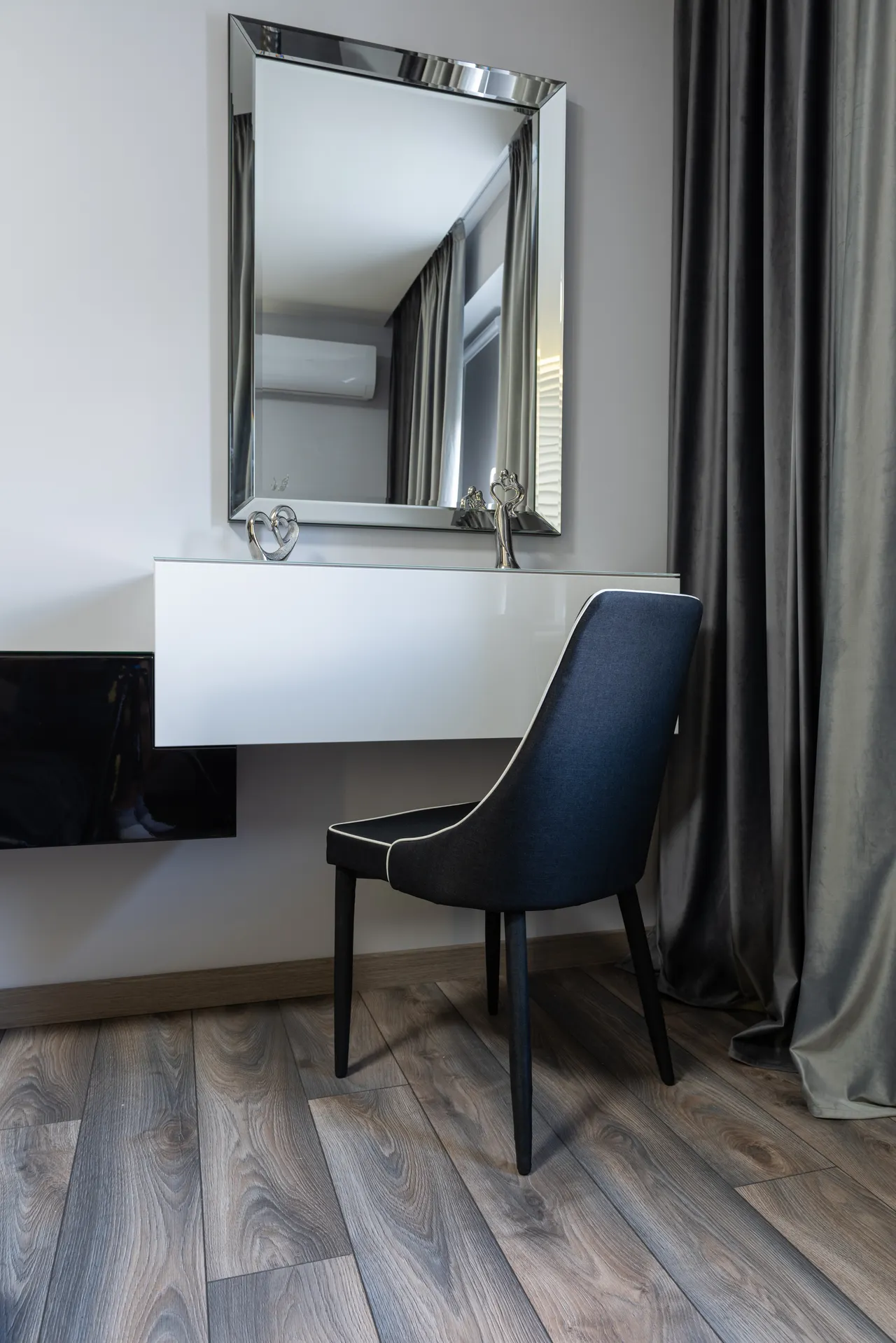 floating-wall-mounted-makeup-vanity-small-bedroom White floating wall-mounted vanity with mirror and dark chair in a small bedroom