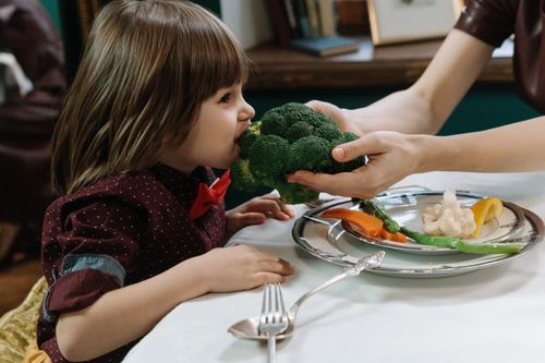 Free Cute child eating broccoli, promoting healthy eating habits indoors. Stock Photo