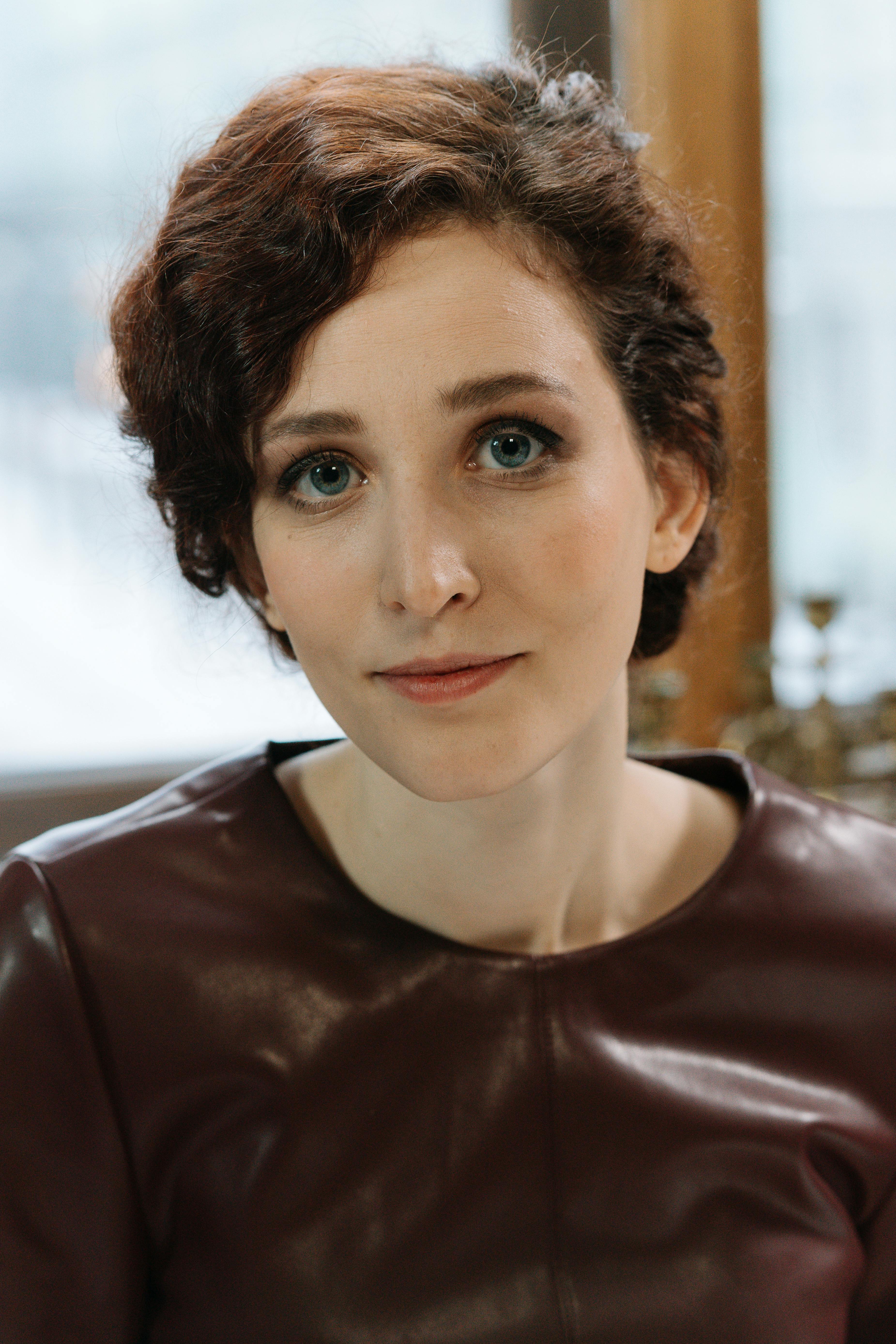Charming portrait of a smiling woman with short curly hair in a brown leather top indoors.