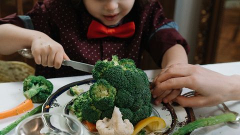 Young boy with bowtie delightfully eating a meal of fresh vegetables, emphasizing wholesome childhood dining.