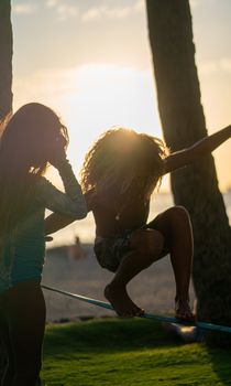 Faceless female with curly hair hunkering down and strolling on rope between trees in lush summer park