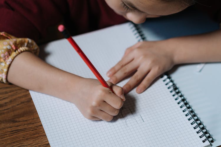 A Kid Writing On A White Notebook