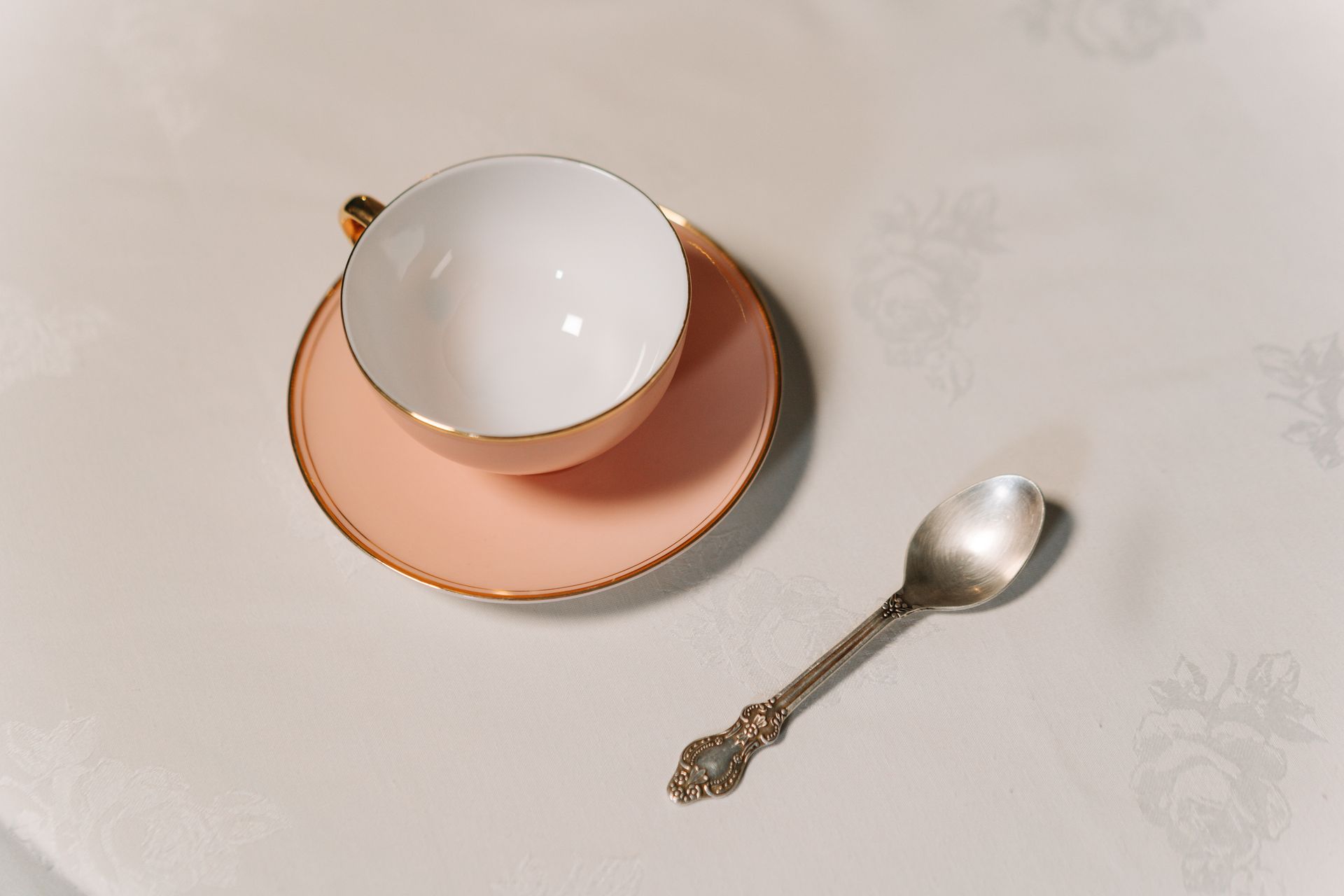 Close-Up Shot of a Cup and Saucer beside a Spoon on a White Table