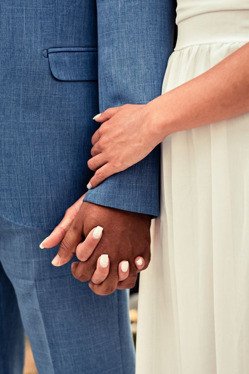 Free Crop unrecognizable multiethnic bride and groom in elegant clothes holding hands at festive event Stock Photo