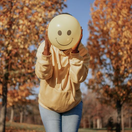 Free Person with smiley balloon in autumn park, exuding joy and playfulness. Stock Photo