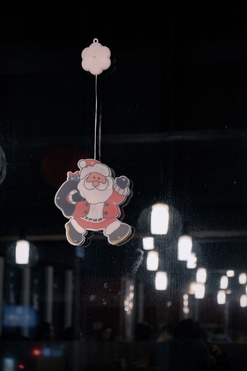 Free Santa ornament hanging on window reflecting indoor lights, festive ambiance. Stock Photo