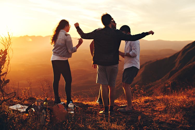 Four Person Standing At Top Of Grassy Mountain