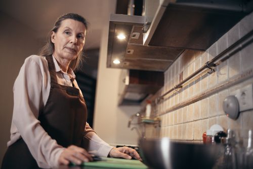 Free A mature woman in an apron stands confidently in a modern kitchen interior. Stock Photo