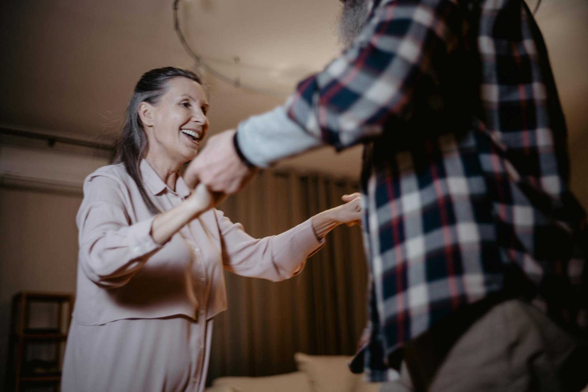 Senior couple enjoying a fun dance together, smiling and holding hands indoors.