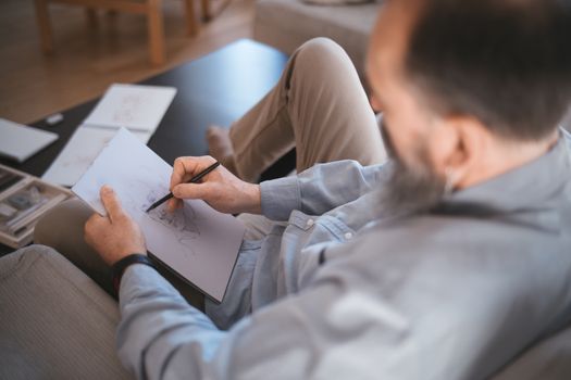 A relaxed man sketching on paper in a cozy room, showcasing creativity and leisure.