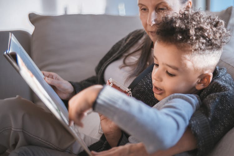 A Kid Reading A Book With His Grandmother