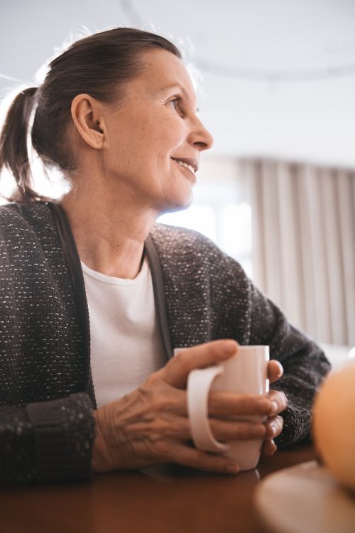 Free Senior woman holding a mug, smiling and enjoying a warm drink indoors. Stock Photo
