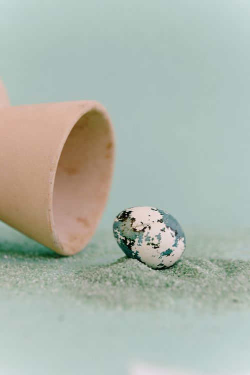 Free A speckled egg balances on sand with an upside-down vase beside it. Stock Photo