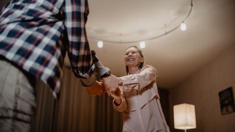 A happy senior couple dancing joyfully indoors, embracing a moment of togetherness.