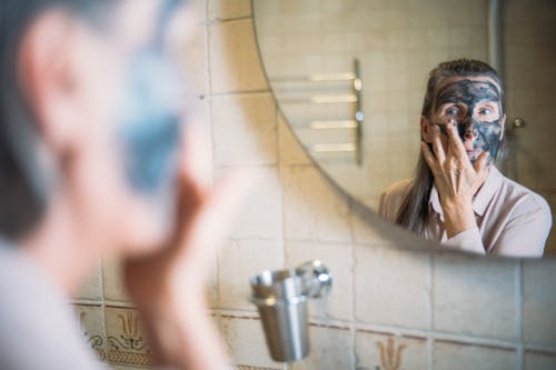 Free Woman in the Mirror Image Applying Black Face Cream Stock Photo
