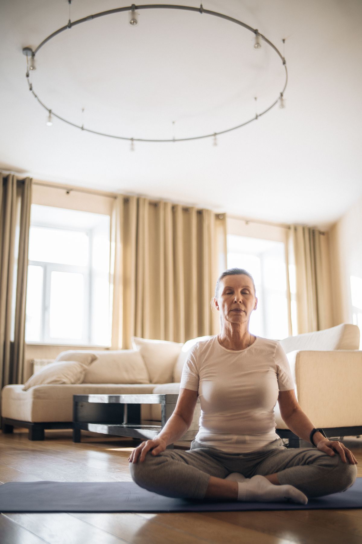 Mature woman practicing yoga on a mat in a cozy living room