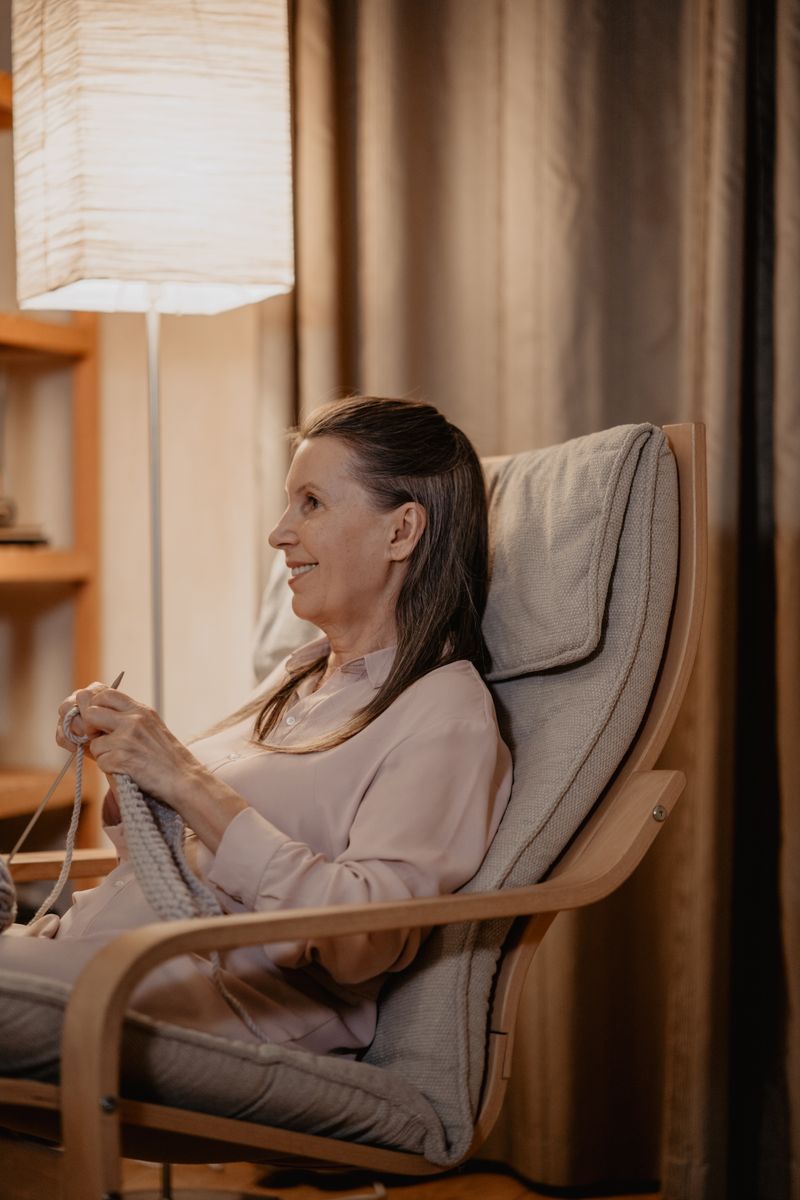 Senior woman enjoys knitting in a cozy home setting, sitting comfortably and smiling.