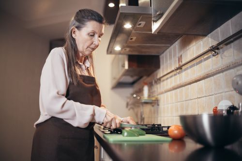 Free Senior woman chopping vegetables in a warm, cozy kitchen setting. Engaged in daily home cooking. Stock Photo