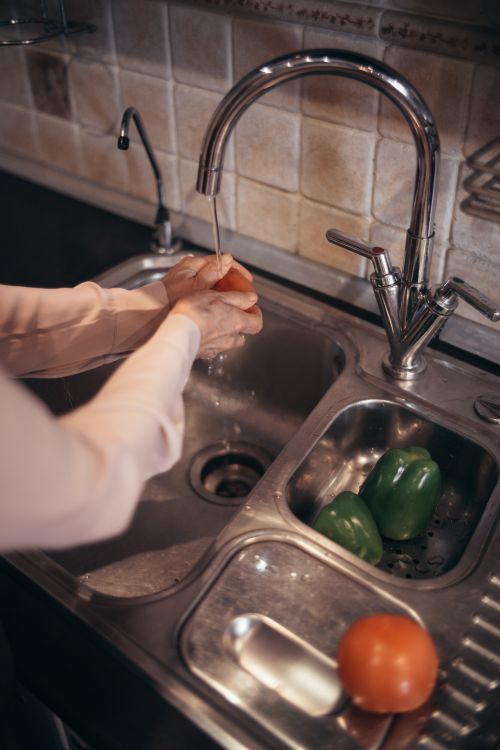 Free Person washing fresh vegetables under running tap water in a kitchen. Stock Photo