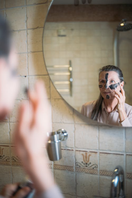 Free Reflection of an Elderly Woman Putting a Charcoal Face Mask on Her Face Stock Photo
