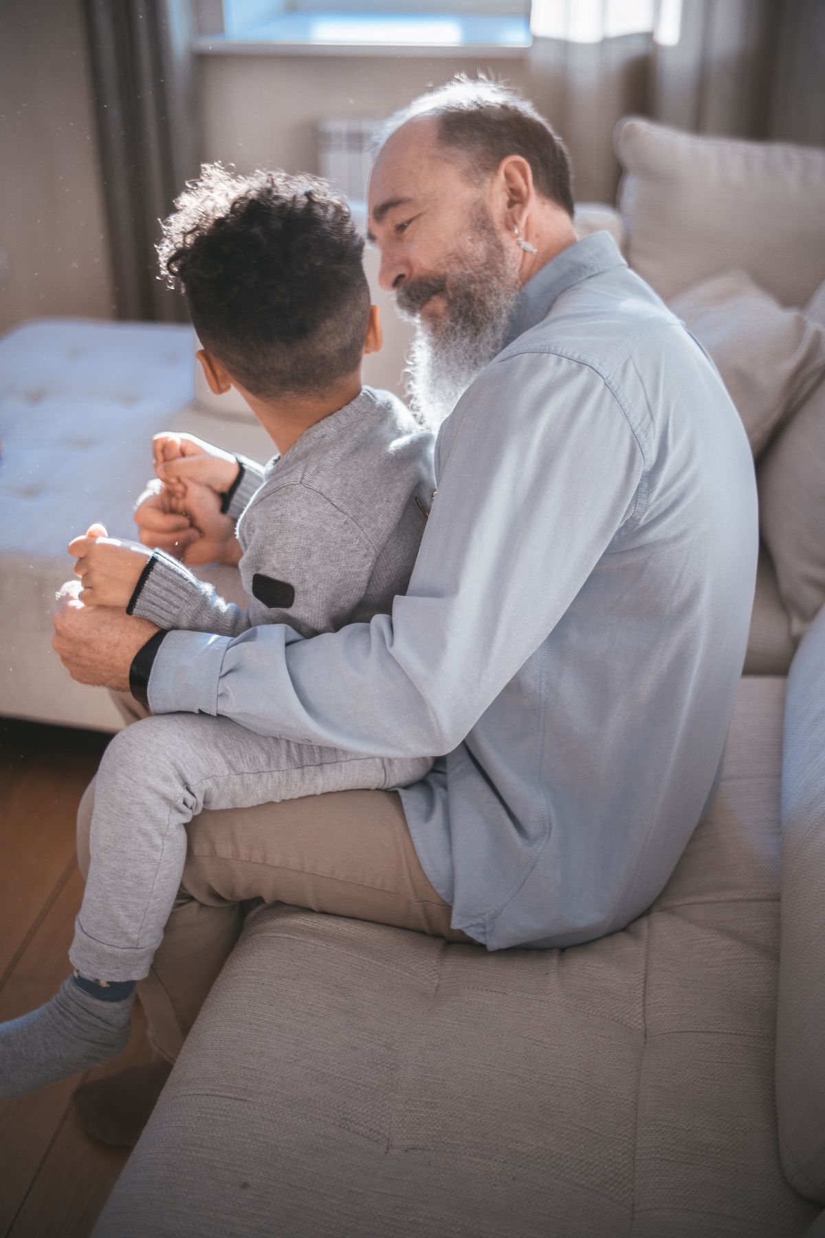 A grandfather holding a young child on his lap on a cozy sofa