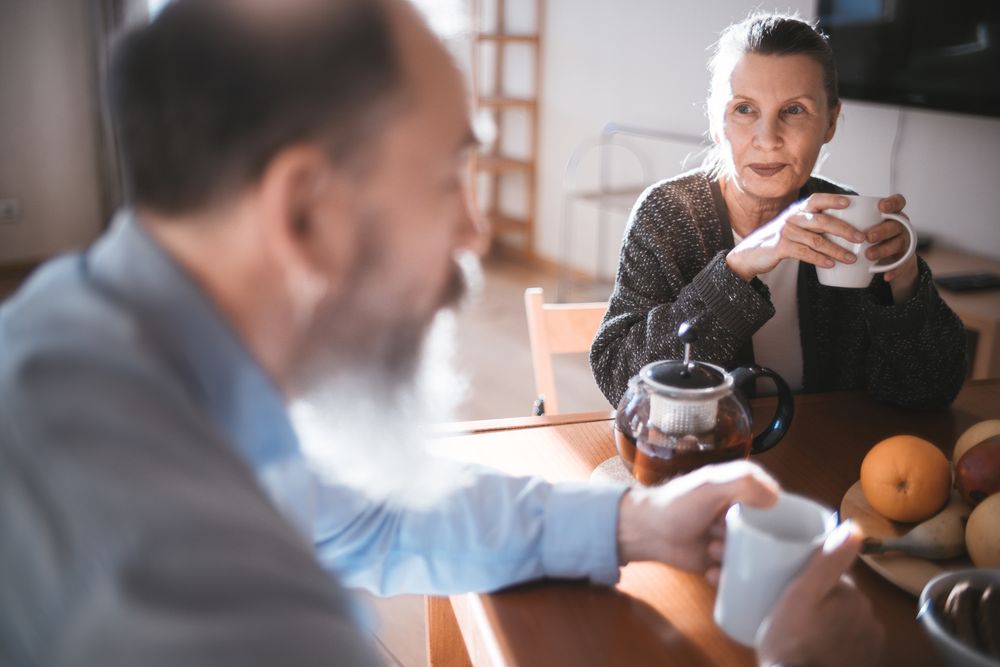 Een ouder iemand drinkt koffie aan de keukentafel, in een rustig moment