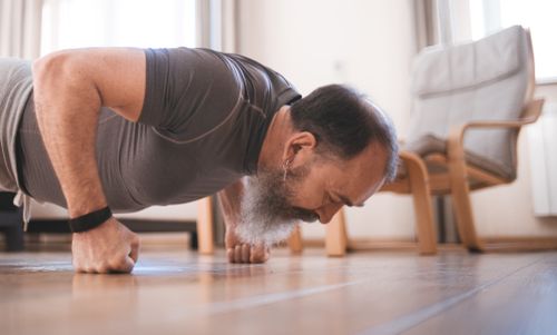 Free Elderly man exercising indoors with push-ups on a wooden floor for fitness. Stock Photo