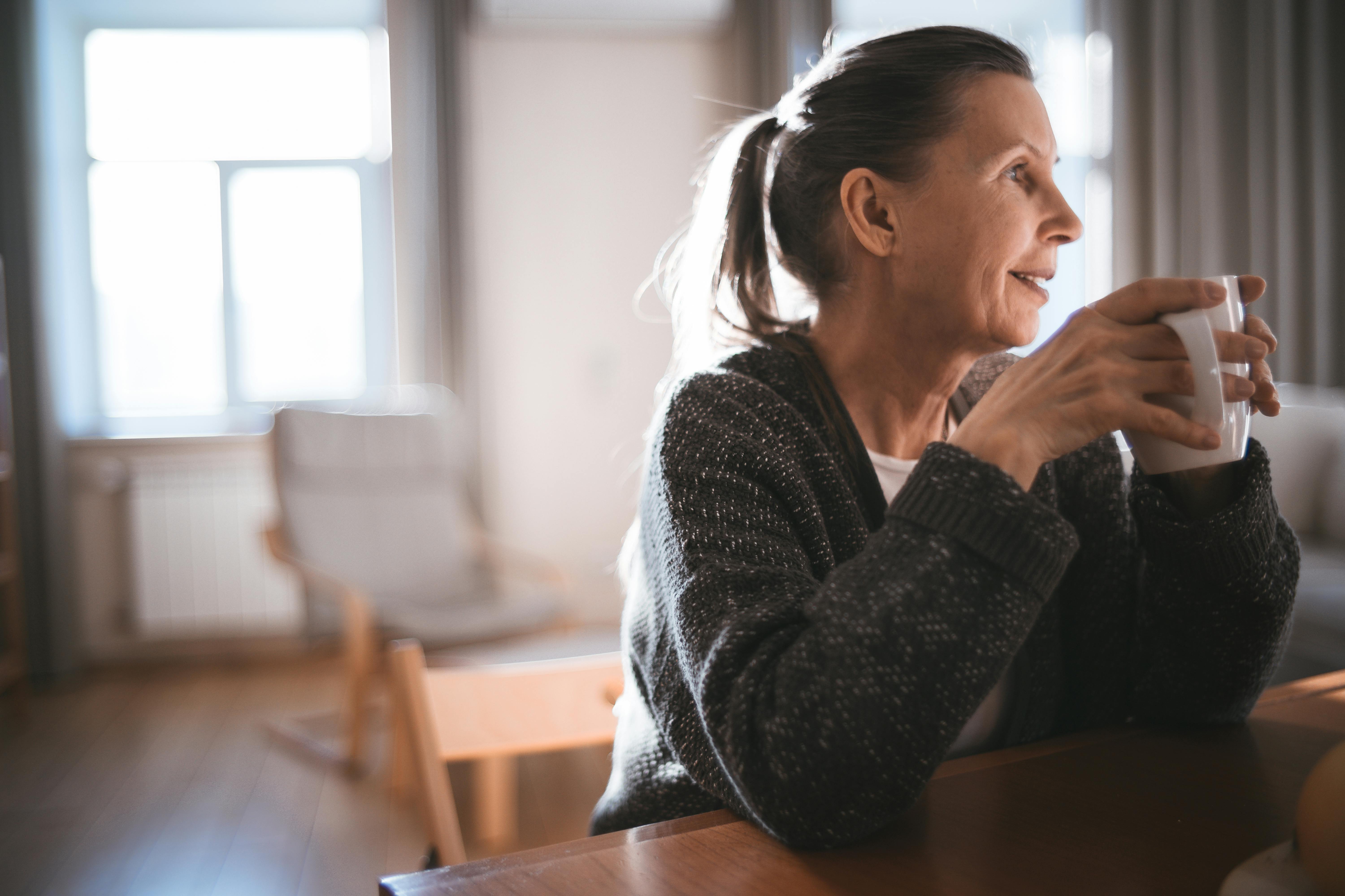 woman in black sweater holding a white ceramic cup