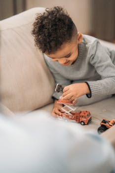 A young boy joyfully playing with toy fire trucks and cars inside a cozy room.
