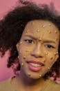 Resentful African American female teenager with yellow stars sequins on face looking at camera on pink background in modern studio