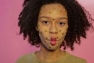 Young African American female with yellow star rhinestones on face looking at camera while making fish lips on pink background
