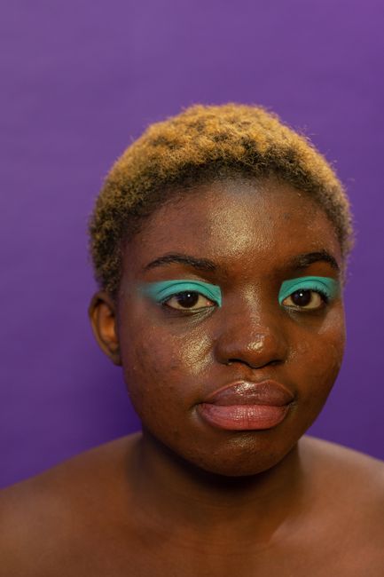 Portrait of African American female model with bright makeup and dyed hair looking at camera on purple background in studio