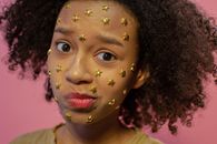 Stylish African American female teenager with abundance of yellow decorative stars on face looking at camera and making face on pink background