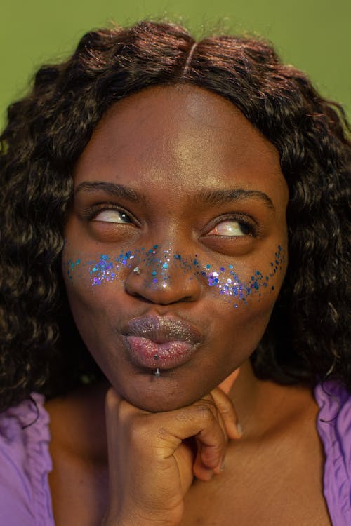 Free Eccentric crop African American female with piercing touching chin and having fun while looking away on green background Stock Photo