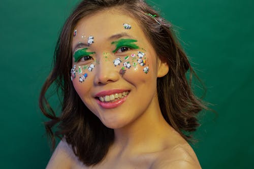 Crop positive ethnic female with bright makeup smiling and looking at camera on green background of studio