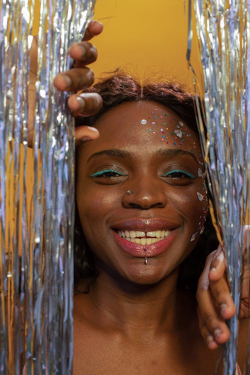 Glad African American female with green eyeliner smiling and looking at camera on yellow background