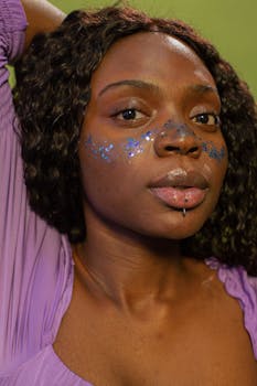 Close-up portrait of a woman with glitter makeup, showcasing curly hair and a vibrant expression.