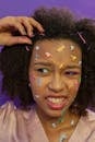 African American female teenager in pajama with various colorful animal stickers on face and hairpins in curly hair and makeup on purple background in light studio