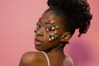 Confident young black woman with multicolored fluffy small balls on face looking over shoulder in bight studio on pink background