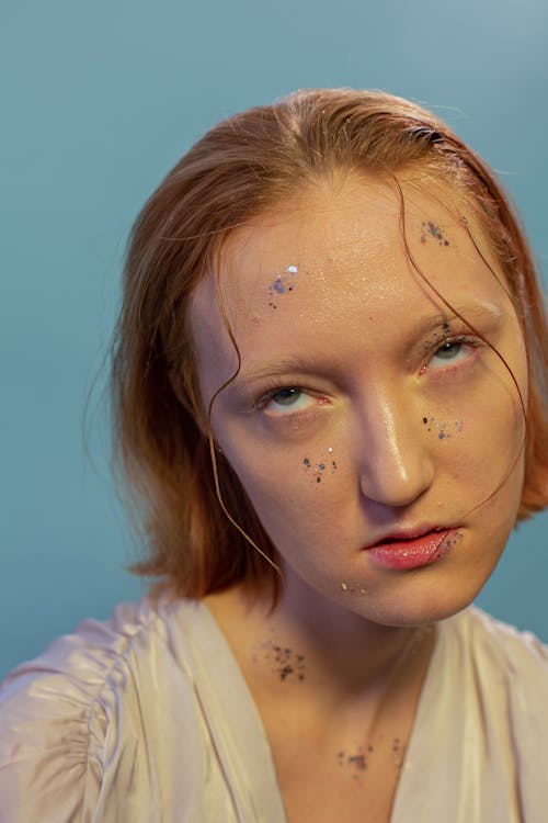 Free Tired young woman with shimmering glitters on face in bight studio on blue background Stock Photo