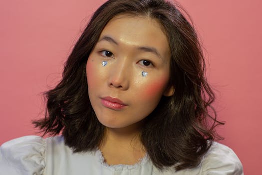Close-up portrait of a woman with heart-shaped makeup on cheeks against a pink background.