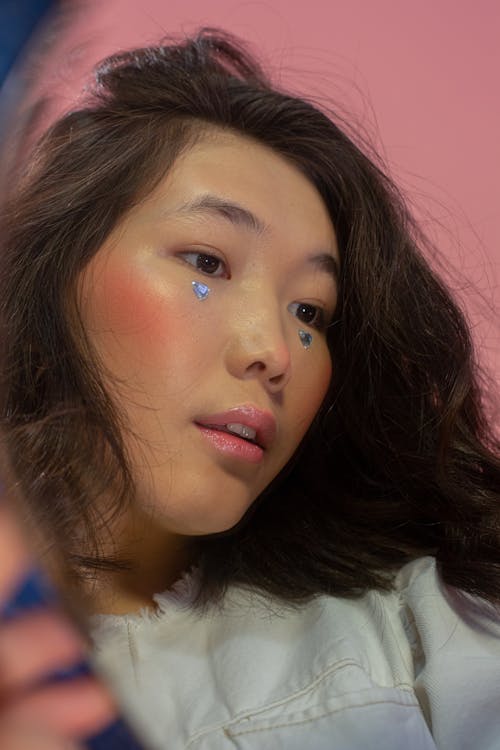 Calm ethnic woman with dark hair looking away in pink studio