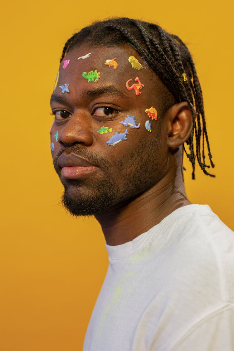 Trendy Young Ethnic Guy With Colorful Face Stickers Looking At Camera Against Yellow Background