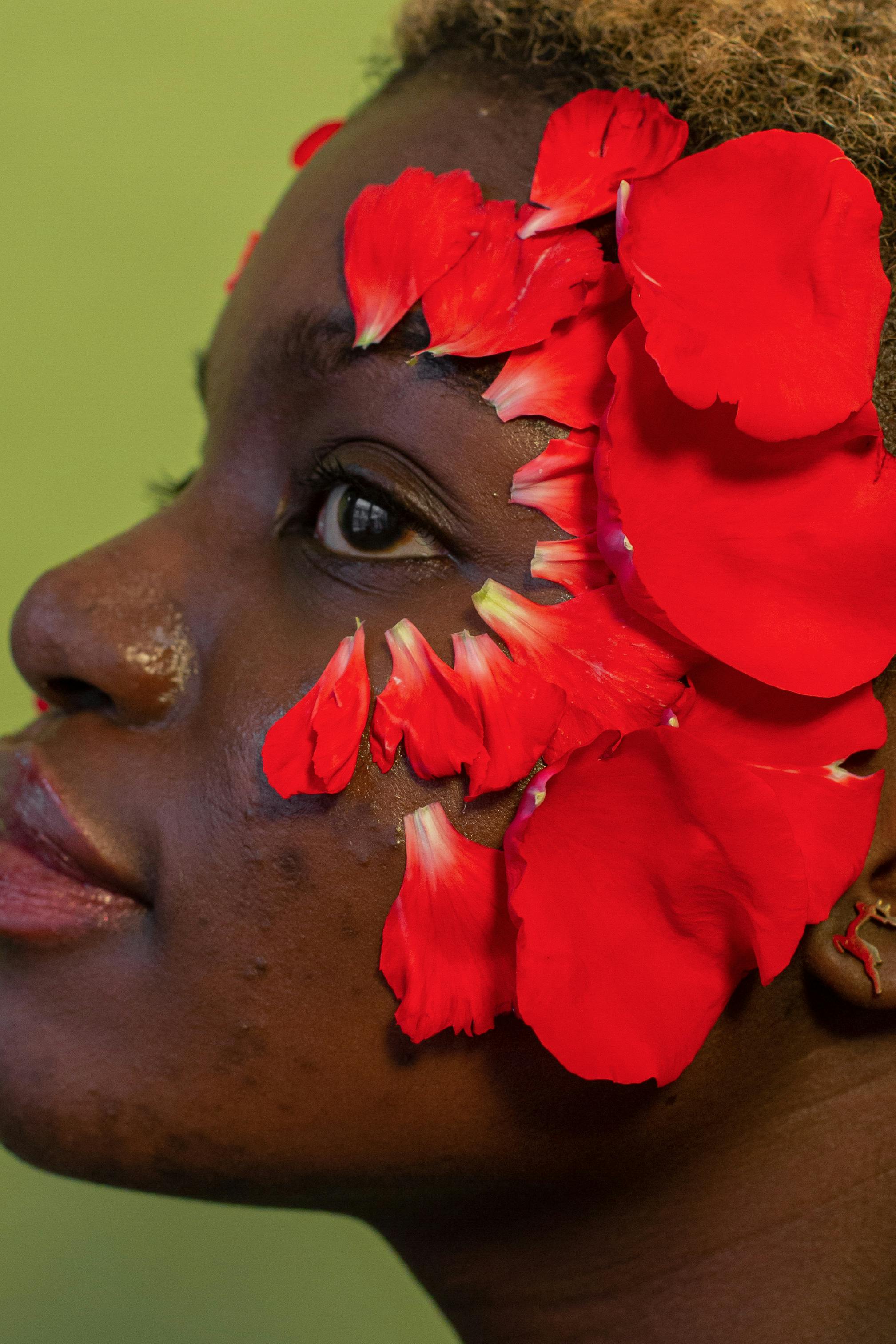 crop unemotional black woman with red petals on face