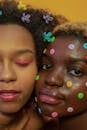 Crop African American female models with bright makeup and colorful buttons on face and multicolored vivid clasps in hair